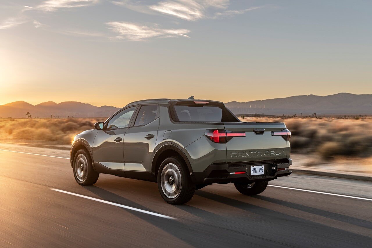 A photo of a Santa Cruz Pickup Truck driving on a desert road with mountains in the background.
