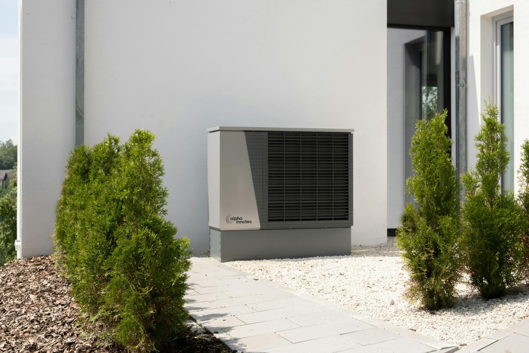 An outdoor HVAC system on the side of a building with a small shrub next to it.
