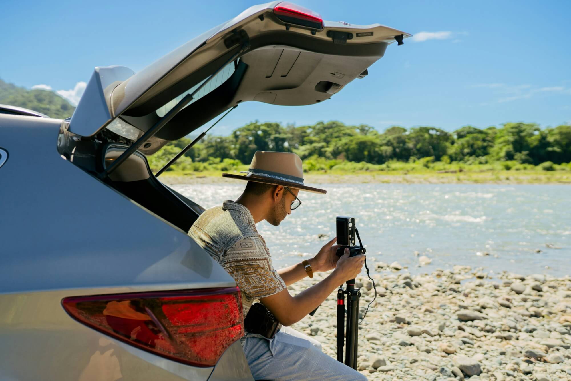 A person sitting in the trunk of a SUV that is parked on a river. The person is getting ready to go fishing.