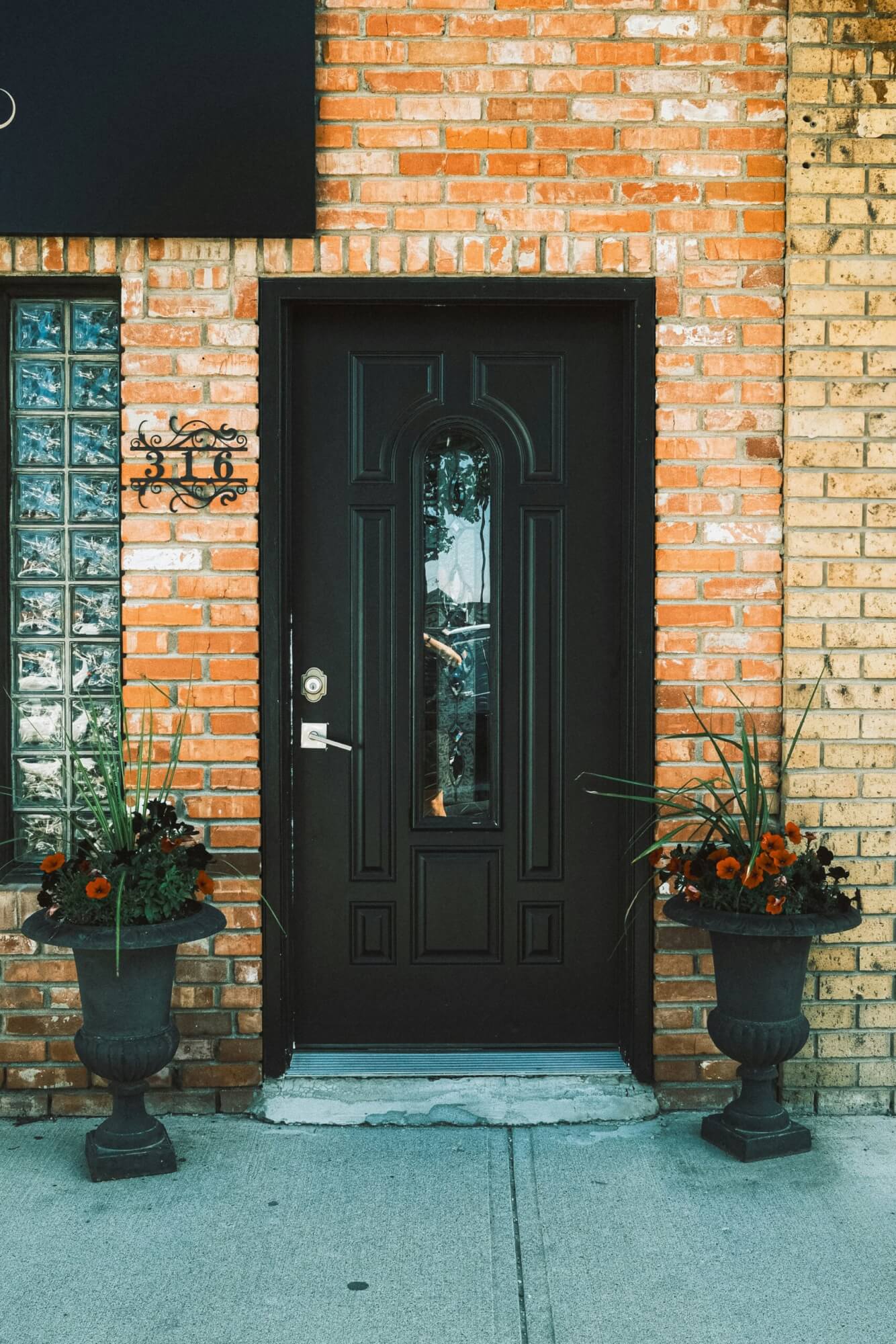 A brick building with a black exterior door framed by 2 potted plants.