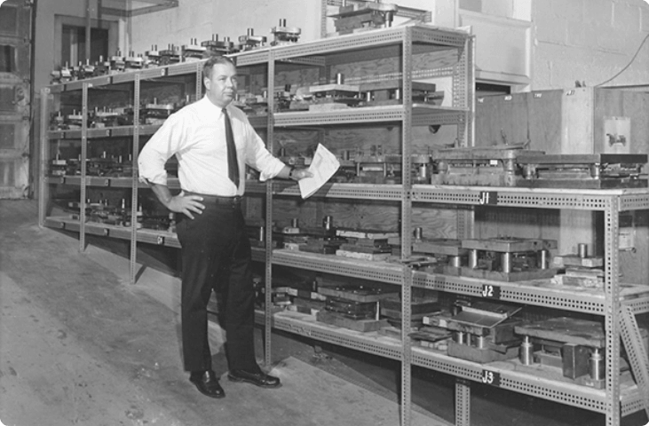 A person standing in an old manufacturing facility leaning against open shelves.