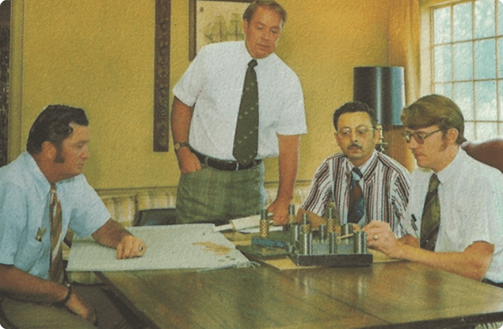 Four people standing around a conference room table looking over documents.