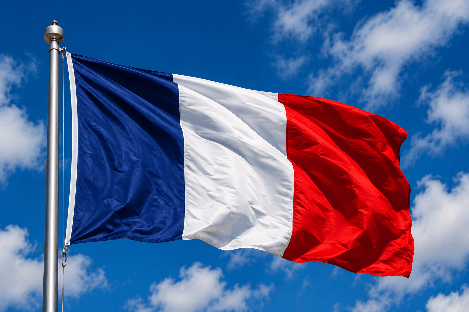 A picture of a French flag blowing in the breeze with a blue sky and clouds in the background.
