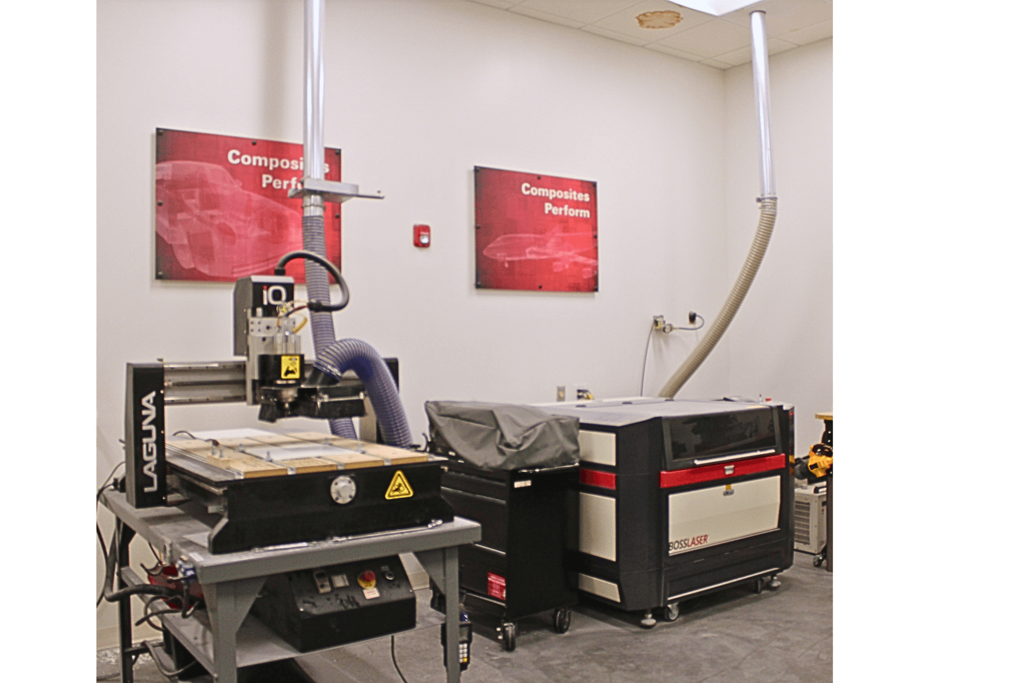 A picture of two different machines in a manufacturing lab. One is a laser cutter and the other is a CNC cutter. On the wall are 2 different red signs both saying "composites perform".