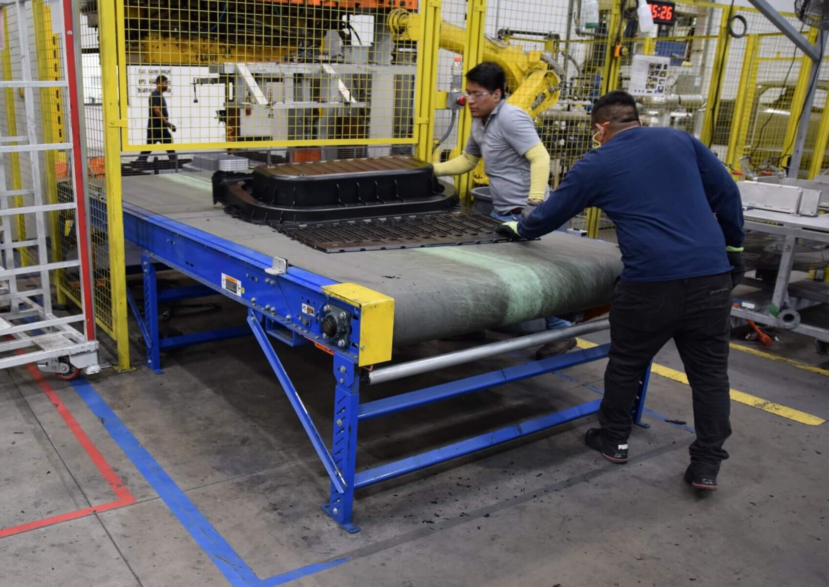 A picture of two people working in a manufacturing plant at the end of a parts line pulling off a finished truck box part.