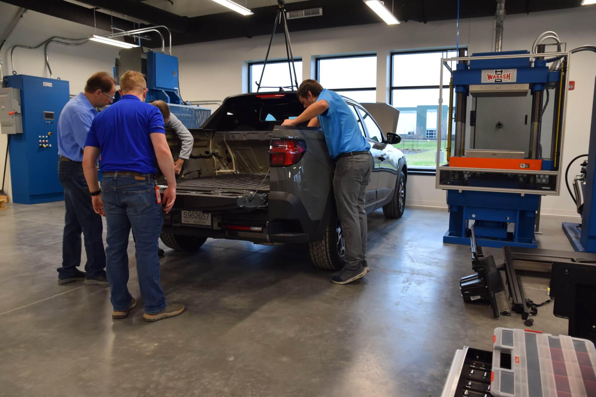 A picture of four people looking at the truck bed of a Hyundai Santa Cruz in an industrial lab.