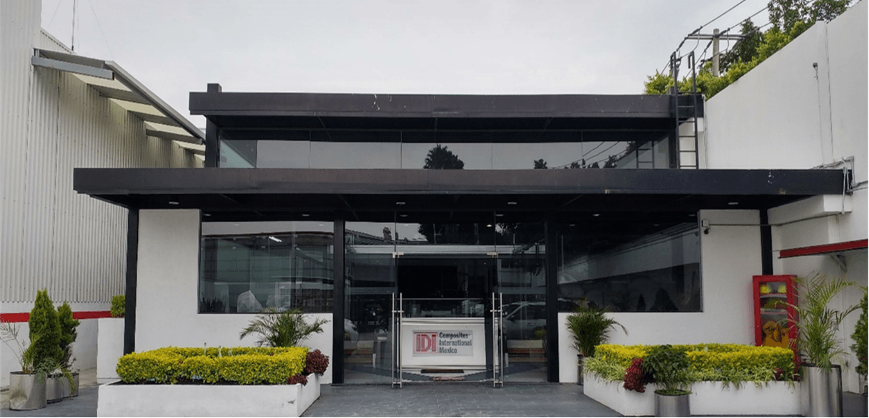 A picture of IDI Composites International's building in Mexico City. It is a white building with green shrubs lining the walkway.