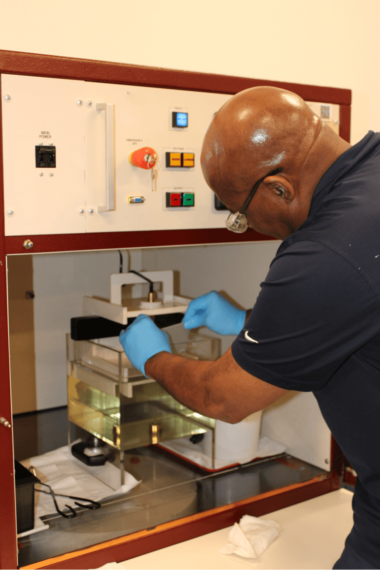A man with blue protective gloves on placing a material into testing equipment.
