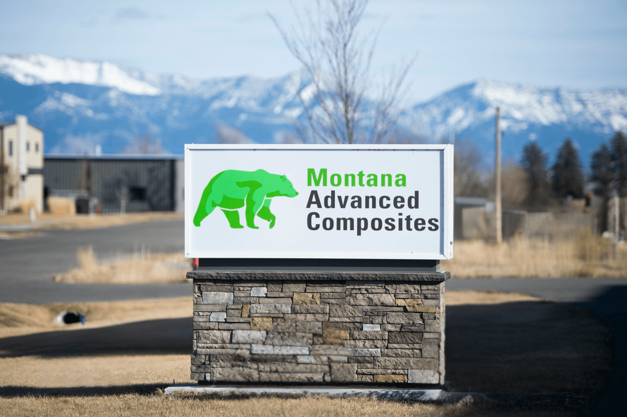 A picture of Montana Advanced Composites' sign with a green bear and the mountains in the background.