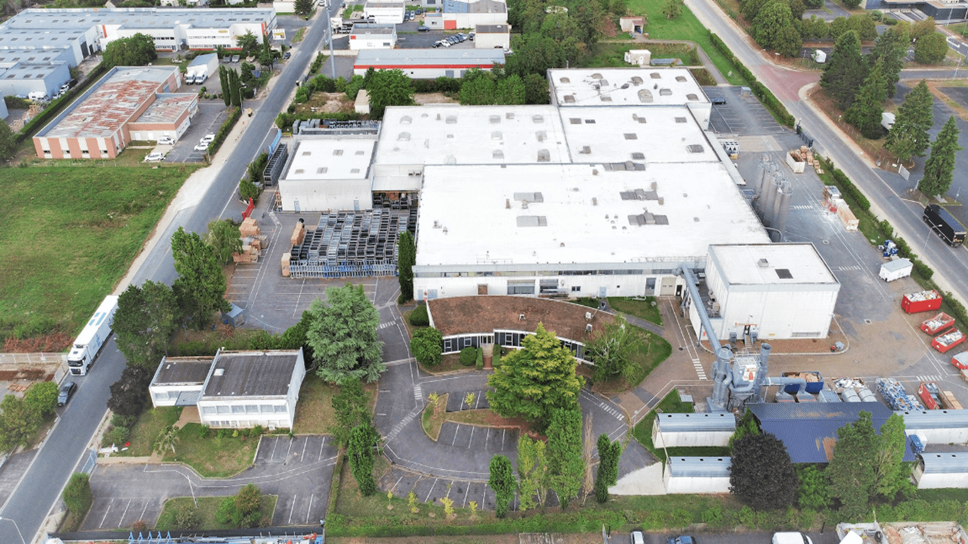 An aerial view of a manufacturing facility with a large parking lot and some grassy areas.