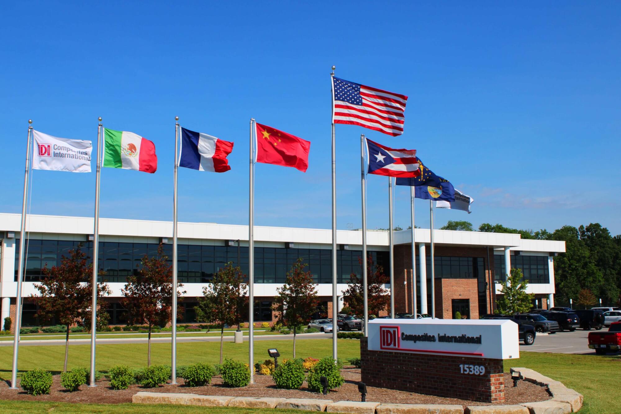 Flags blowing in the wind in front of a large office building with a sign in the front that says IDI Composites International.