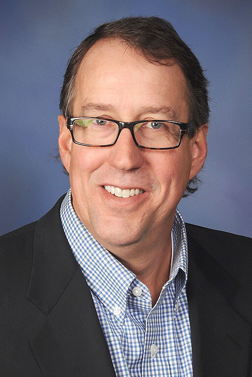 A professional headshot of a man in a black blazer.