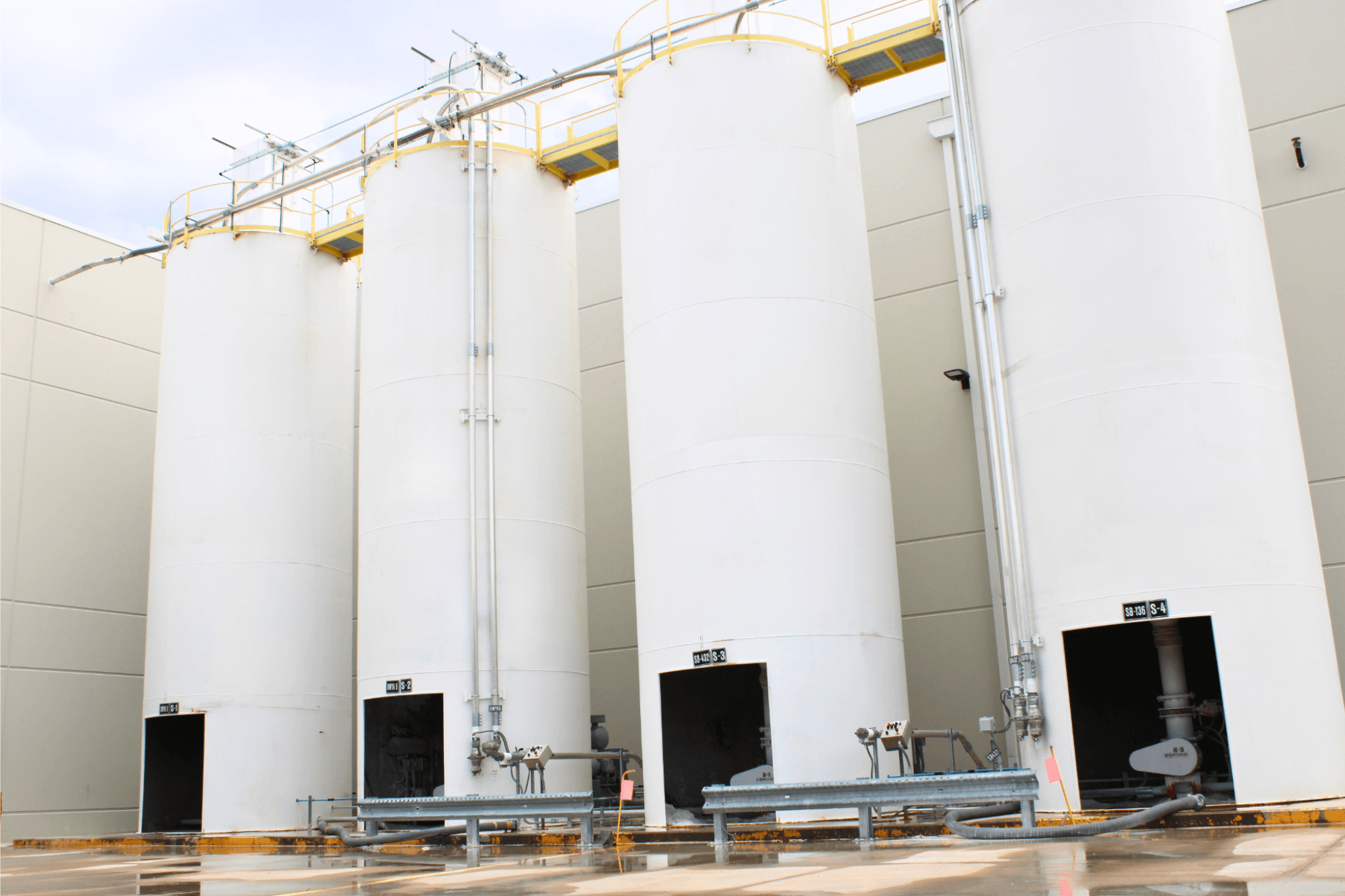 Four white silos outside of a manufacturing facility.